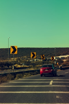 a red car driving down a road next to yellow signs