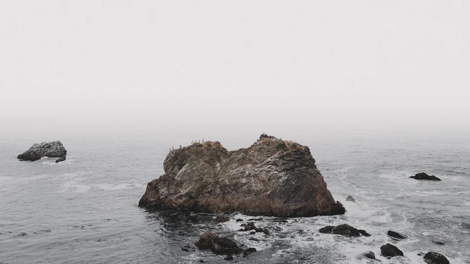 Two large rocks jut out into the ocean, surrounded by small waves and ripples