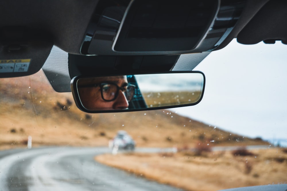 a man with glasses is seen in the rear view mirror of a car