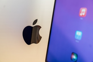 A close-up view of a computer screen displaying app icons on a blue background, next to a metallic surface with an Apple logo.