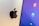 A close-up view of a computer screen displaying app icons on a blue background, next to a metallic surface with an Apple logo.