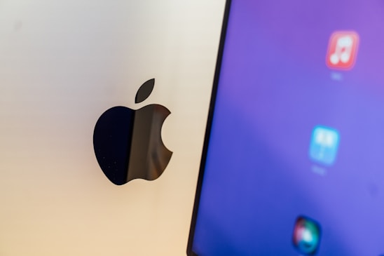 A close-up view of a computer screen displaying app icons on a blue background, next to a metallic surface with an Apple logo.