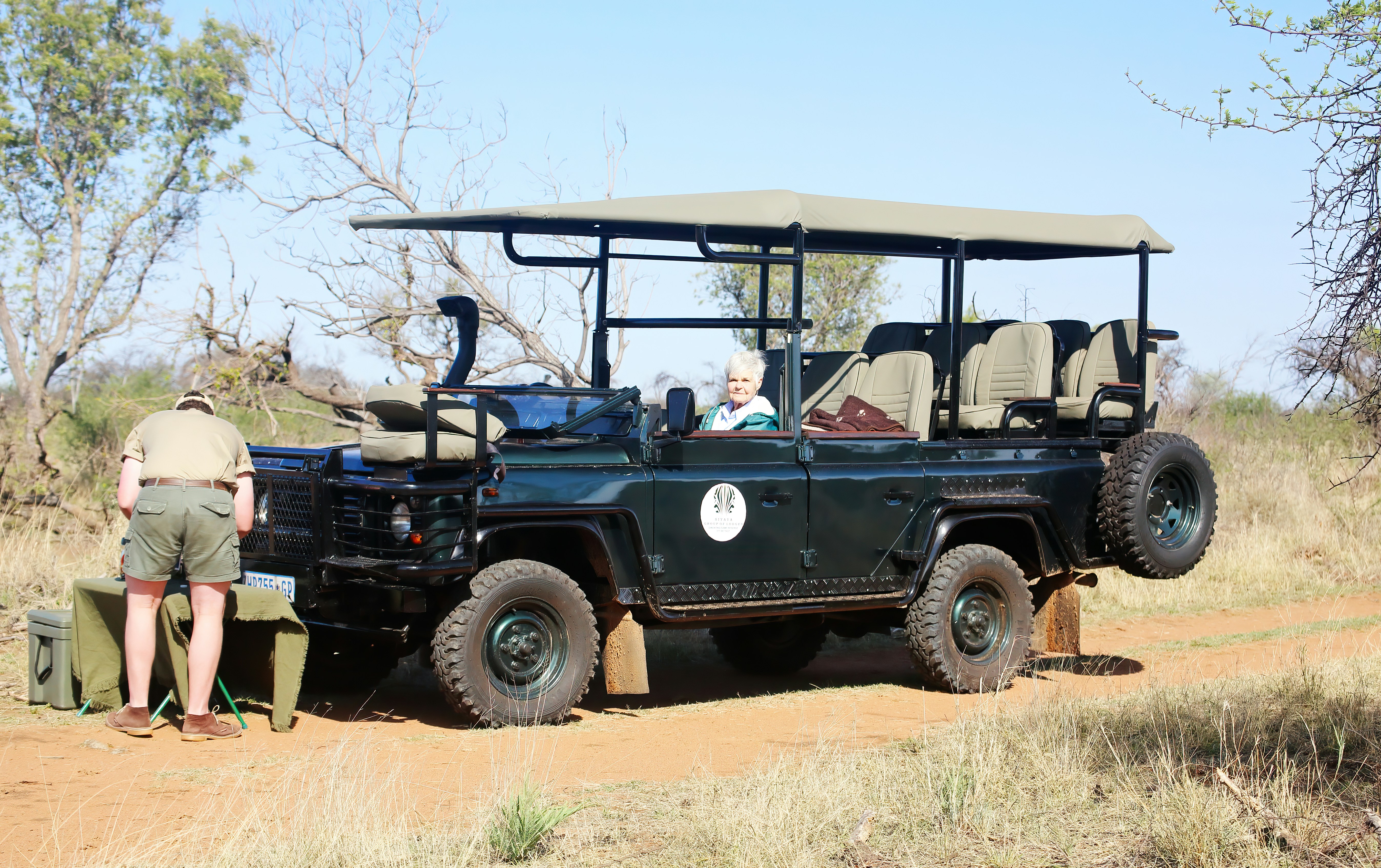 a man standing next to a black jeep on a dirt road, Tea time on Safari