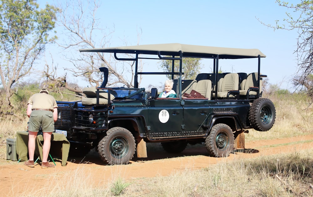 Un hombre parado junto a un jeep negro en un camino de tierra