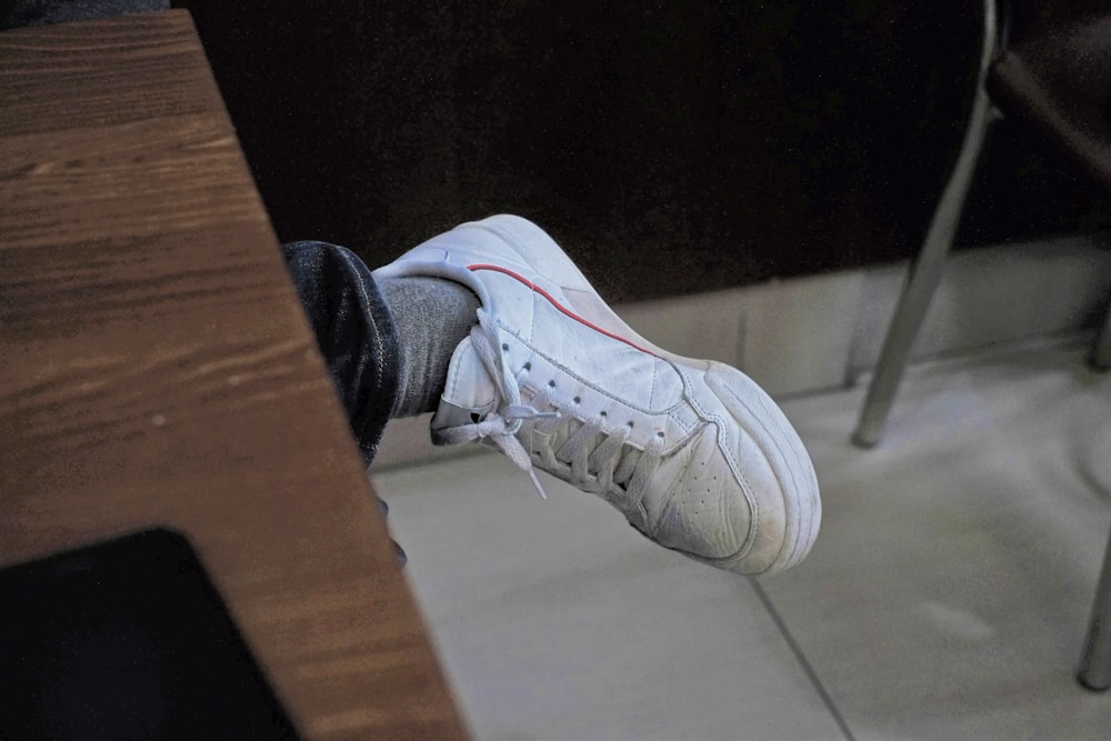 os pés de uma pessoa com tênis brancos em uma mesa de madeira
