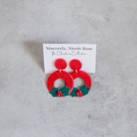 Festive red and green enamel earrings sparkling under warm lighting.
