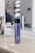 A bottle of MATRIX Total Results So Silver shampoo is placed on a wooden surface. The background features a mirror with reflections and blurred objects, including a person sitting and some salon equipment.
