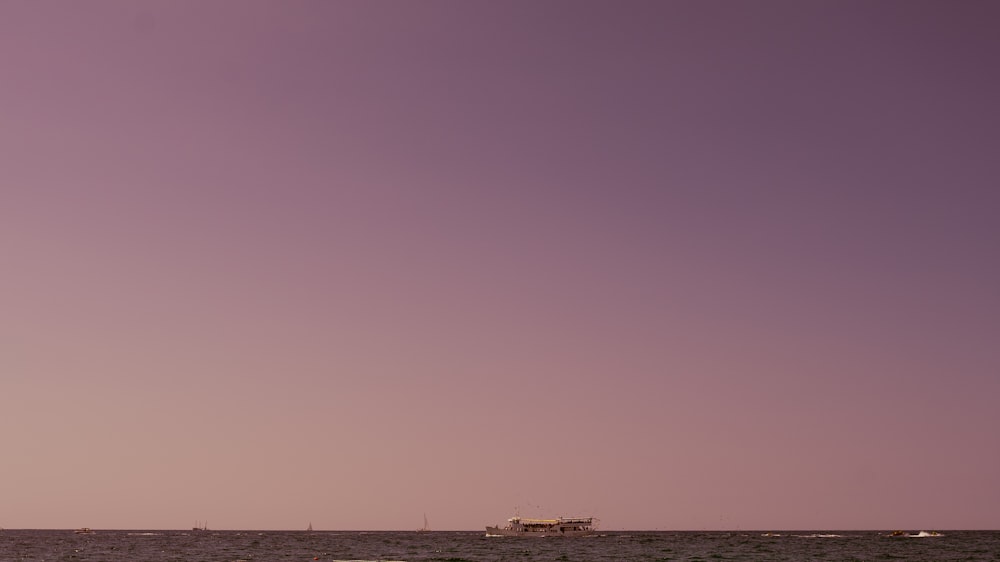 a boat is out on the ocean under a purple sky