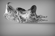 A complex abstract sculpture appears to be floating, featuring a fluid and dynamic form resembling twisted metal or liquid. The piece has flowing, wavy elements that create a sense of movement and fluidity.
