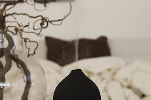 A peaceful bedroom scene with soft pillows, blackout curtains, and a diffuser emitting calming mist.