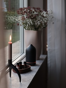 a vase with flowers and candles on a window sill