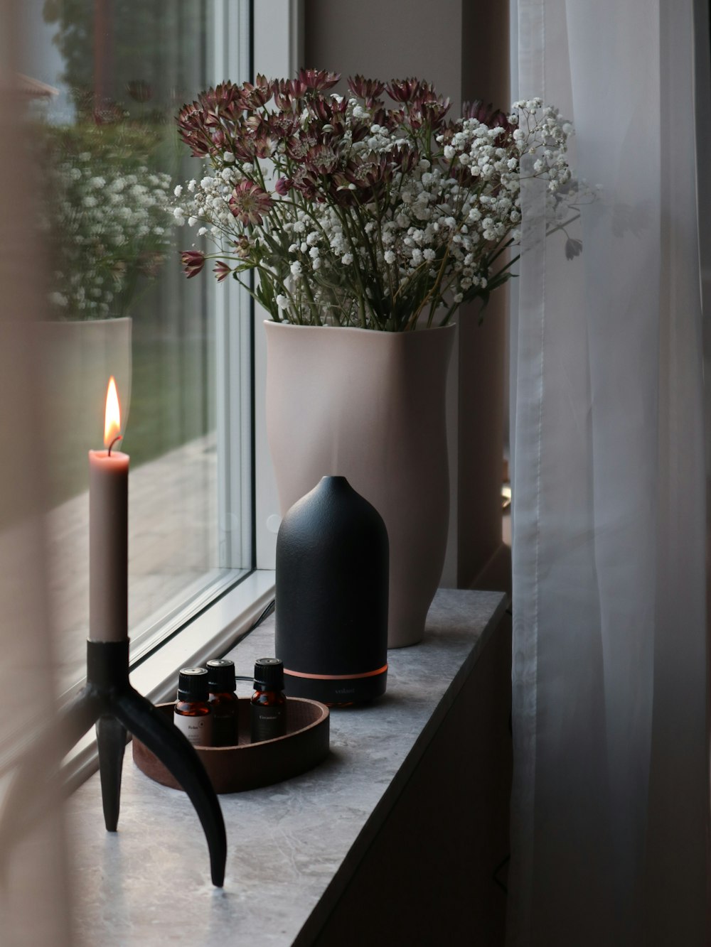 a vase with flowers and candles on a window sill