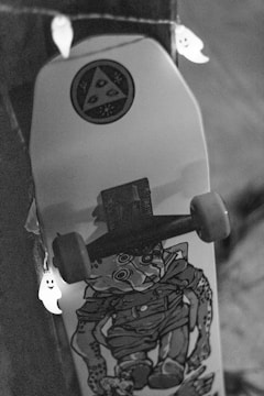 A skateboard with a graphic design featuring a stylized character. It is decorated with a string of small ghost lights, creating a playful and spooky atmosphere. The setting is dimly lit, focusing more on the skateboard and the lights.
