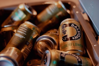 Several cans of Dalston's Elderflower sparkling water are partially seen in a cooler or container. The cans have a gold and black design with some green text, reflecting a modern and vibrant look.