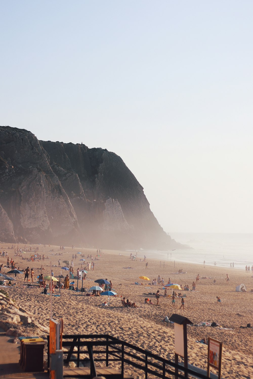 a crowded beach with people and umbrellas on a foggy day