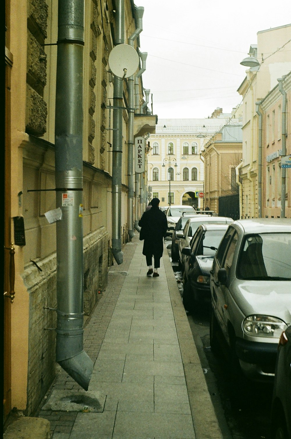 a woman walking down a sidewalk next to parked cars