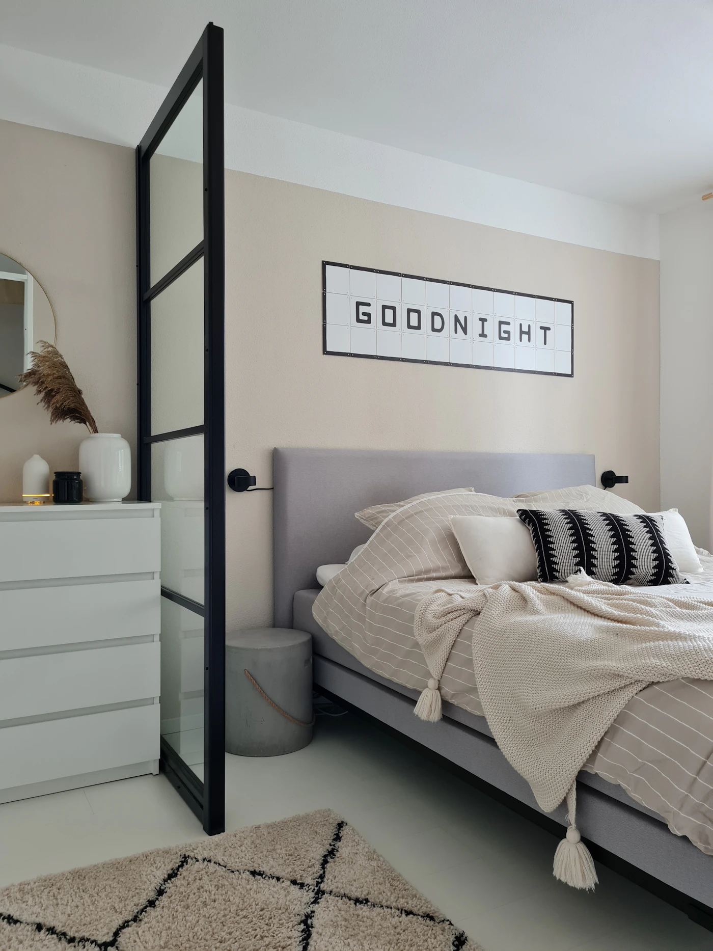Real modern bedroom with an upholstered bed, dresser, mirror, rug, and neutral textiles