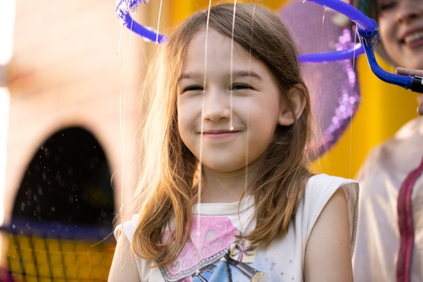 Portrait of a smiling child playing with bubbles against a soft-focus outdoor background.
