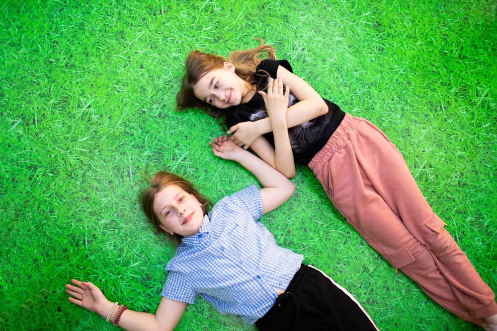 two young girls laying on the grass with their arms around each other