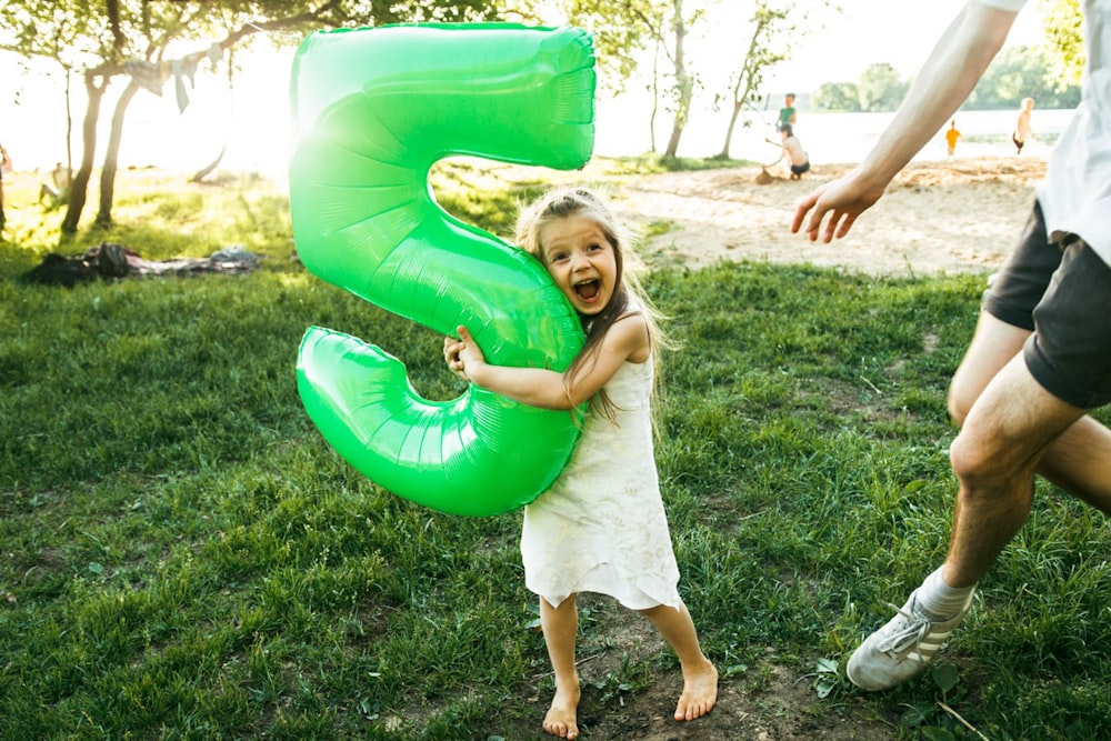 a little girl holding a green number five balloon