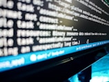 A close-up view of a computer screen displaying lines of code or a terminal output. The text is blurry, but elements like file paths and commands are visible. A blue status bar appears at the bottom of the screen, indicating line and column numbers, along with various settings like spaces and file encoding.