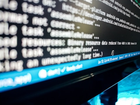 A close-up view of a computer screen displaying lines of code or a terminal output. The text is blurry, but elements like file paths and commands are visible. A blue status bar appears at the bottom of the screen, indicating line and column numbers, along with various settings like spaces and file encoding.