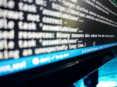 A close-up view of a computer screen displaying lines of code or a terminal output. The text is blurry, but elements like file paths and commands are visible. A blue status bar appears at the bottom of the screen, indicating line and column numbers, along with various settings like spaces and file encoding.