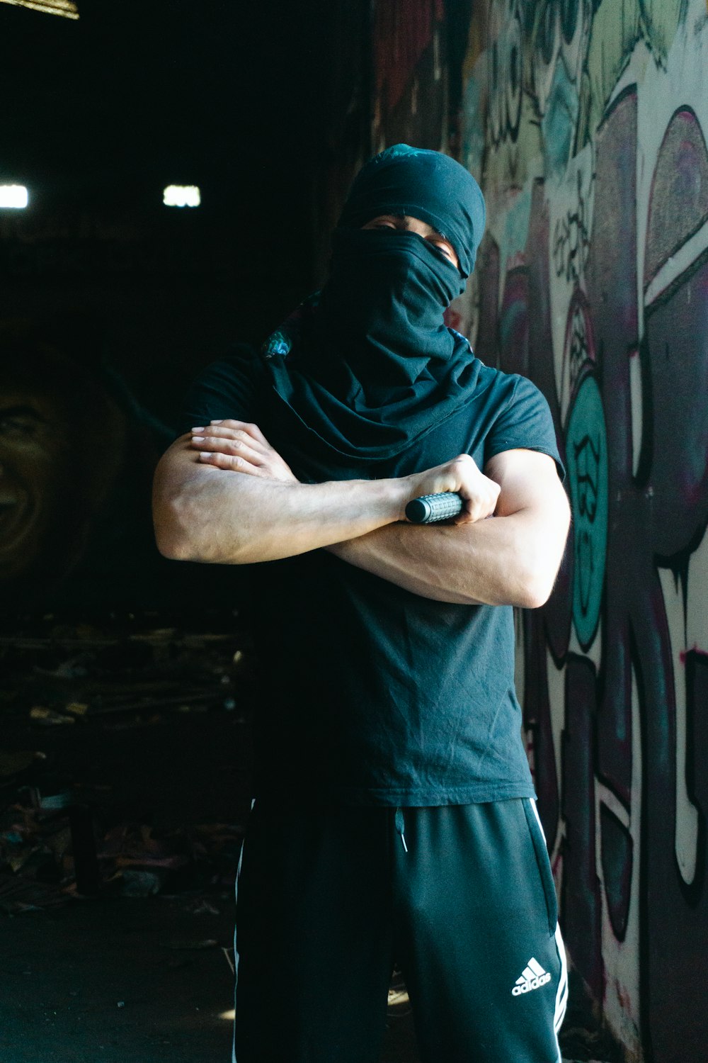 a man wearing a black mask standing in front of a graffiti covered wall