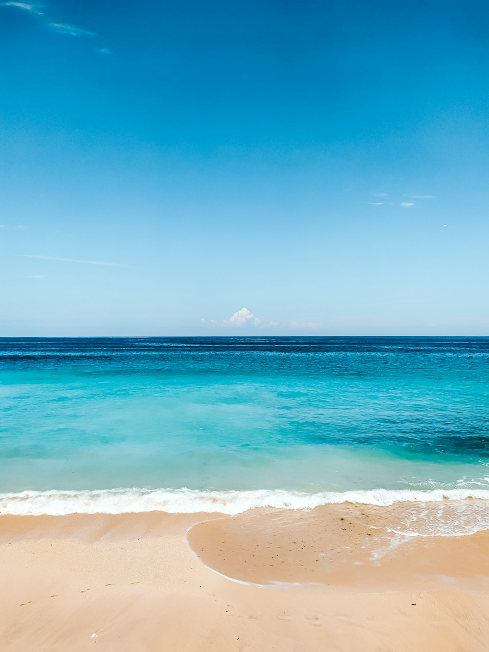 a sandy beach with blue water and a blue sky