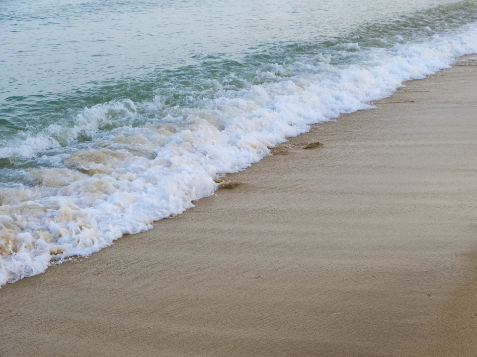 Serene beach scene with beige sand and turquoise water, waves crash on the shoreline