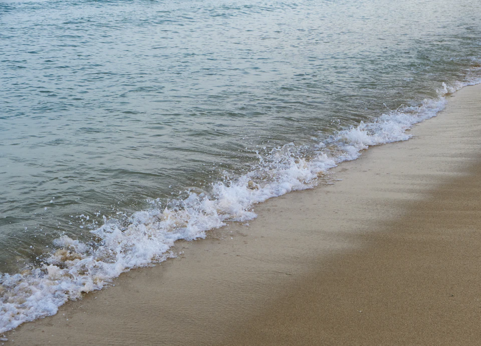 Serene beach scene with beige sand and turquoise water, calm ocean lapping against shore