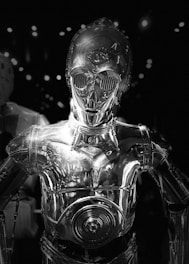 A sleek, metallic humanoid robot with a shiny surface reflecting ambient light. It has large, round eyes and detailed mechanical features, set against a dark background with scattered bright spots.