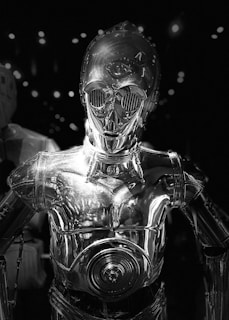 A sleek, metallic humanoid robot with a shiny surface reflecting ambient light. It has large, round eyes and detailed mechanical features, set against a dark background with scattered bright spots.