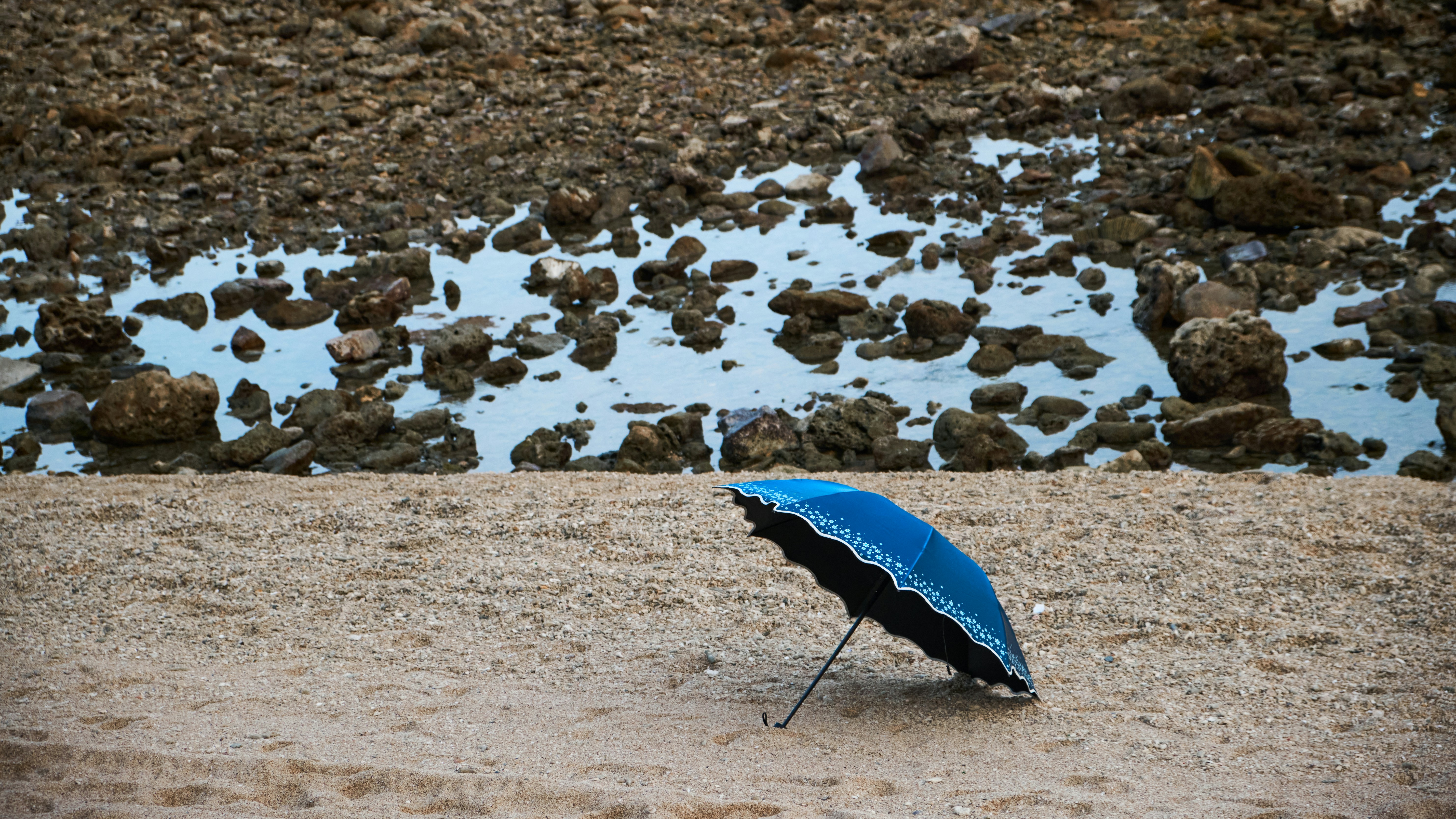 모래 사장 위에 앉아있는 푸른 우산