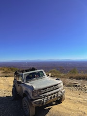 A sleek armored Land Cruiser 300 parked on a rugged mountain path under a clear blue sky.