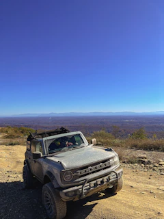 Off-road vehicle parked on a dusty path with dramatic rock spires rising against a bright blue sky.