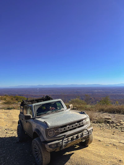 A rugged Mahindra Thar 4x4 parked on a scenic mountain trail under a clear blue sky.