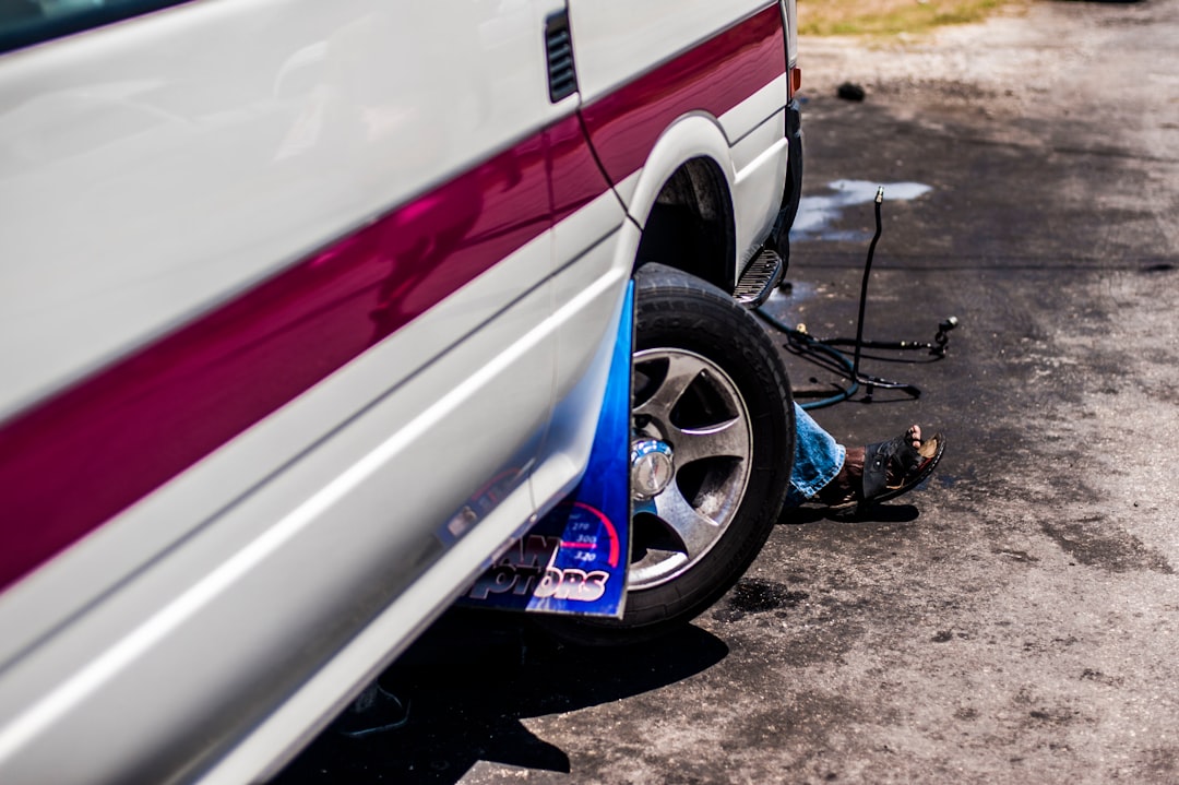 a man sitting on the ground next to a parked car,