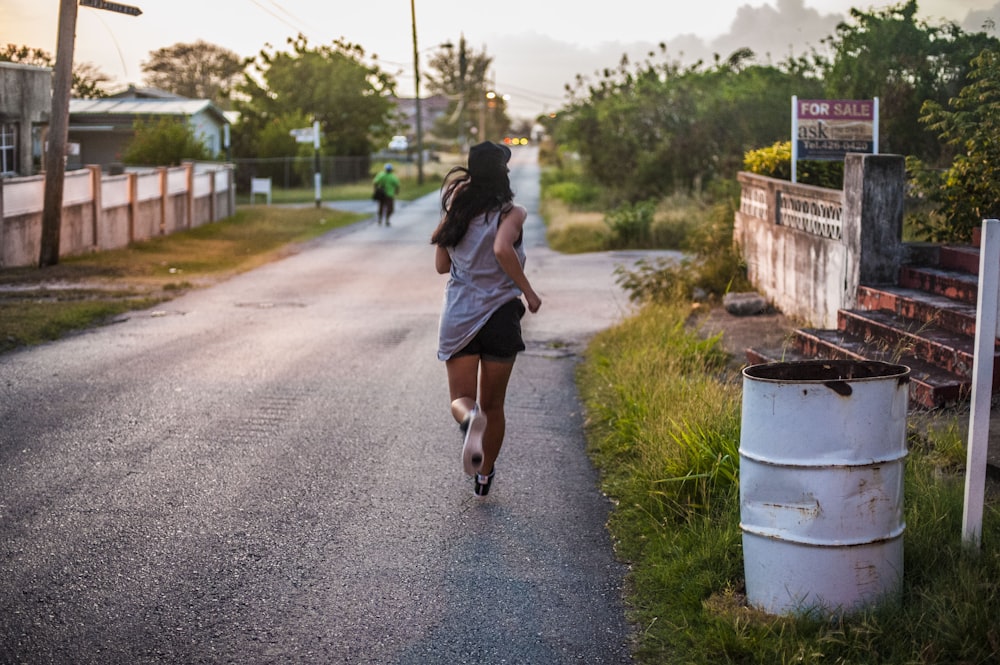 a woman running down a street next to a trash can