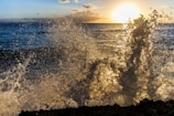 the sun is setting over the ocean and the waves are crashing