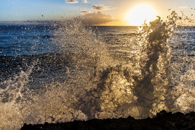 the sun is setting over the ocean and the waves are crashing