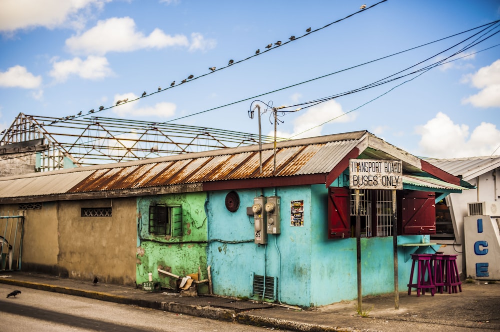 a blue building with a rusted roof and red shutters