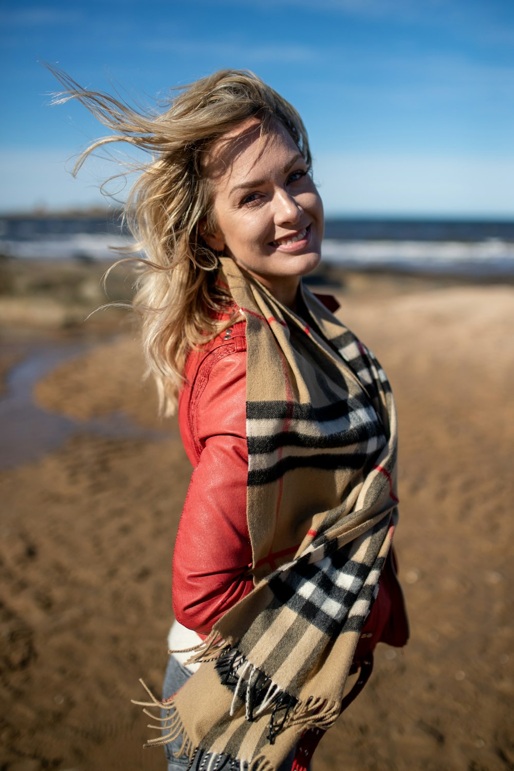 a woman standing on a beach with a scarf around her neck