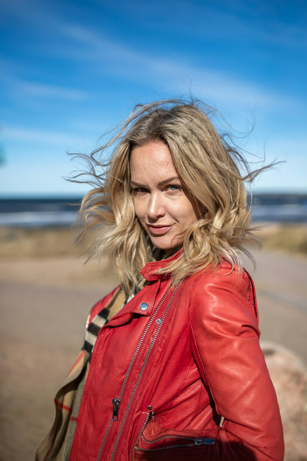 a woman in a red leather jacket standing on the beach