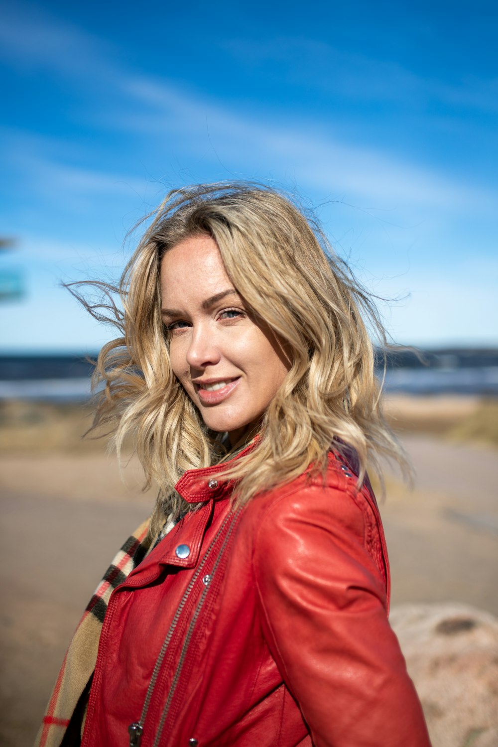 a woman in a red leather jacket standing on a beach