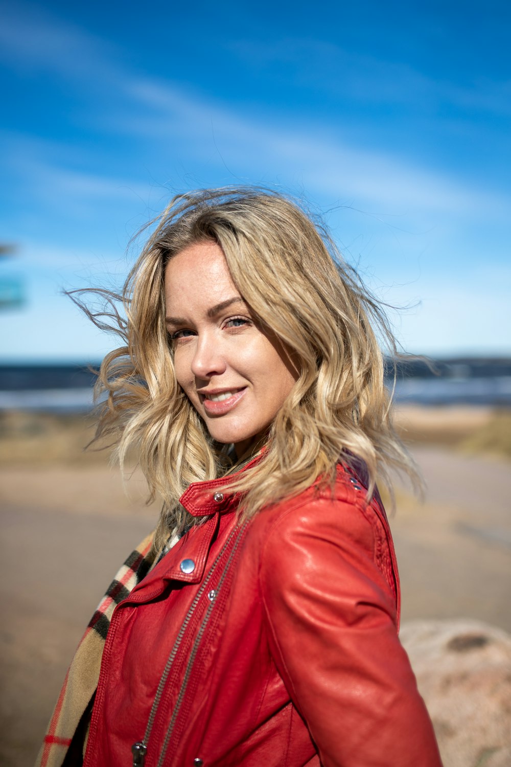 Eine Frau in roter Lederjacke steht am Strand