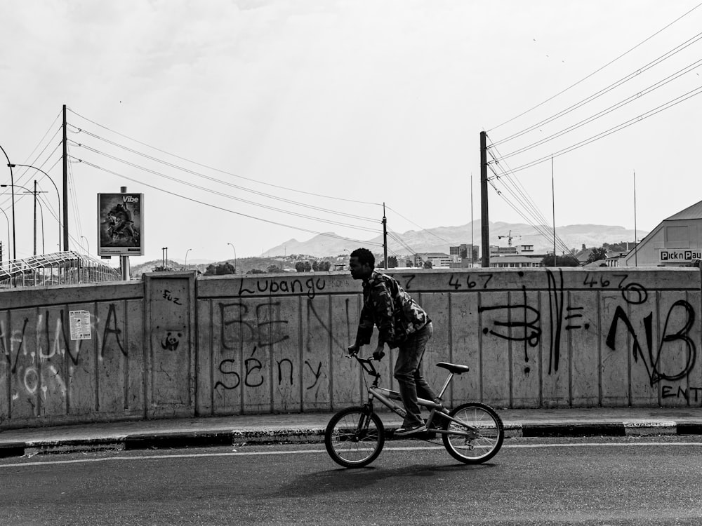 a man riding a bike down a street next to a wall