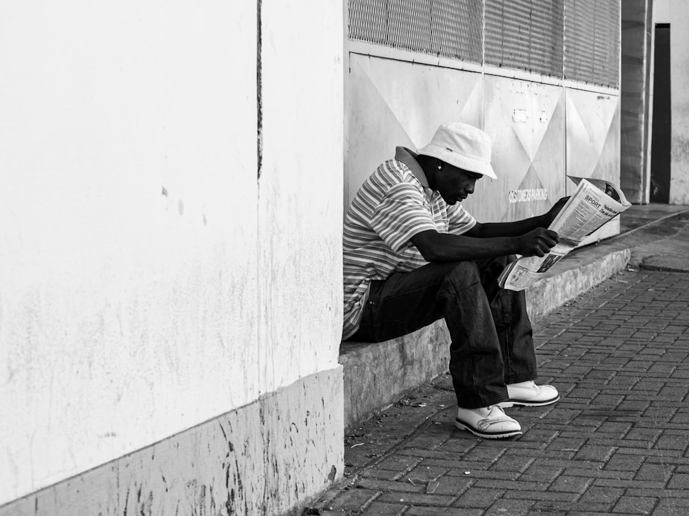 a man sitting on the side of a building reading a newspaper