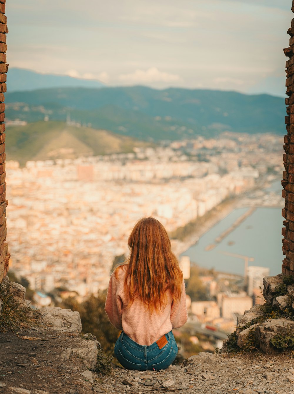 a woman sitting on a ledge looking out over a city