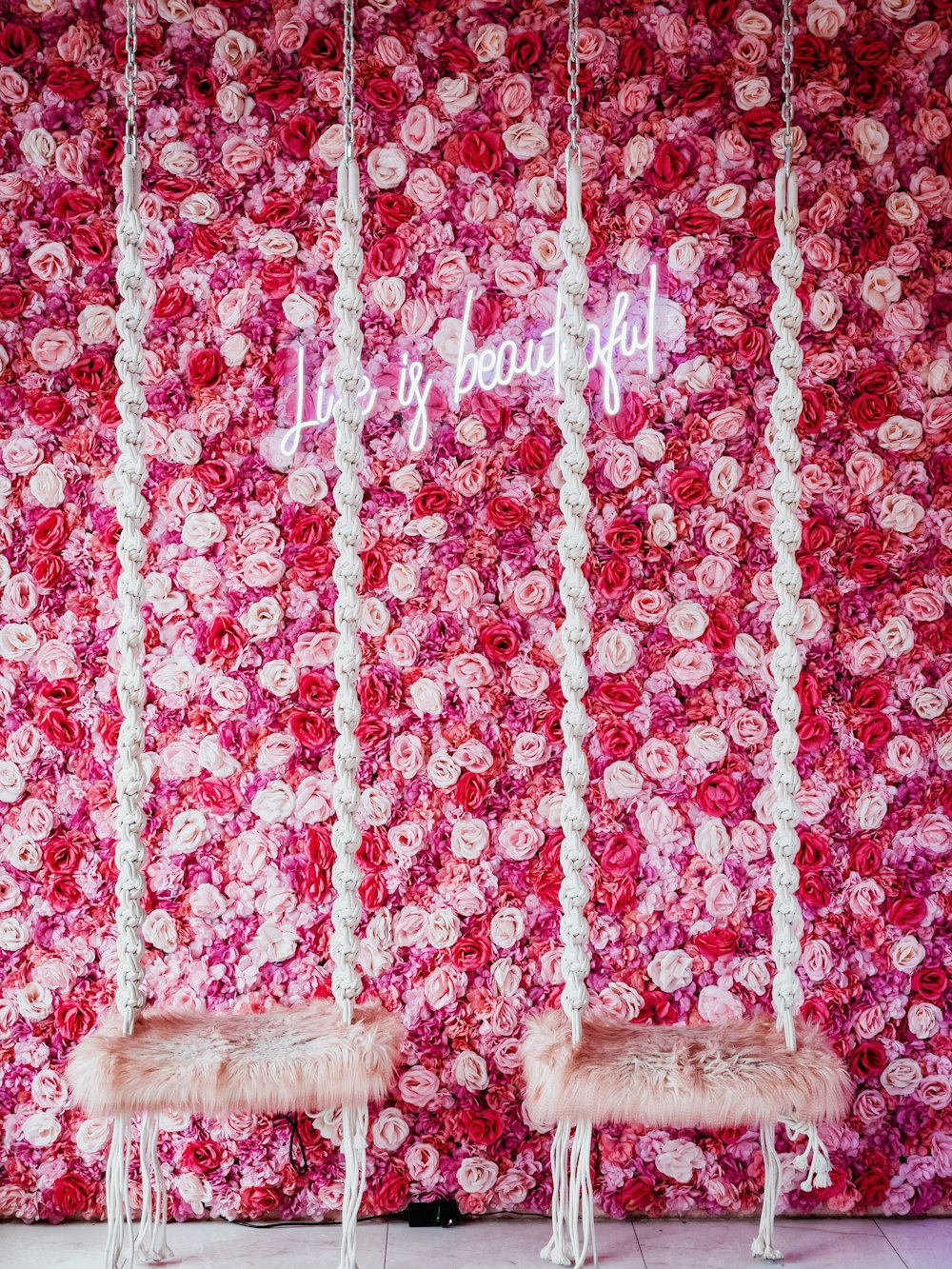 Deux chaises blanches assises devant un mur de fleurs roses